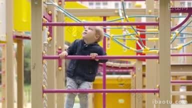 可爱的小男孩在儿童游乐场爬上攀爬架的金属栏杆